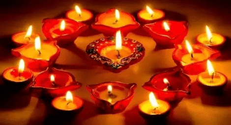 A Circle Of Lit Oil Lamps (Diyas) With A Decorative Diya In The Centre, Arranged On A Dark Surface.