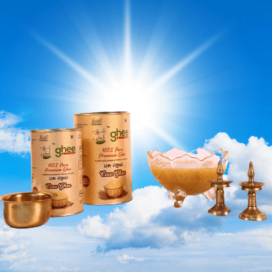 Two Cans Of Ghee, A Brass Bowl, A Decorative Glass Bowl Filled With Ghee, And Two Brass Oil Lamps Against A Backdrop Of A Bright Sky With Clouds.