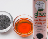 A Bottle Of Ghee Store Cold Pressed Gingelly Oil Is Placed Beside A Bowl Of Black Sesame Seeds And A Bowl Of The Oil.